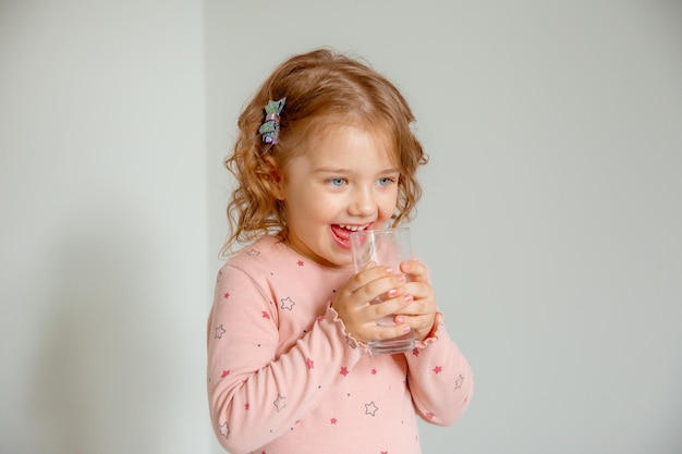 Een klein meisje thuis houdt een glas water vast aanbevolen