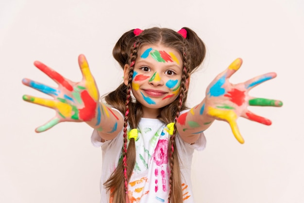 Een klein meisje toont haar handpalmen beschilderd met veelkleurige verf en glimlacht Een schoolmeisje tekent met haar eigen handen Creatieve opvoeding van kinderen Witte geïsoleerde achtergrond