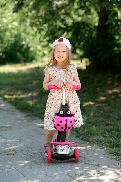 Een klein meisje van 3 jaar oud met een roze pet rijdt op een scooter Zomertijd