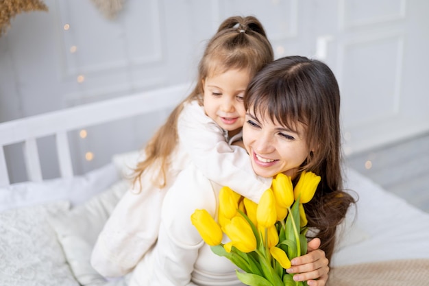 Een klein meisje van een kind met haar moeder knuffel en kus die een boeket gele tulpen geeft lifestyle verse bloemen internationale vrouwendag of moederdag hoogwaardige fotografie