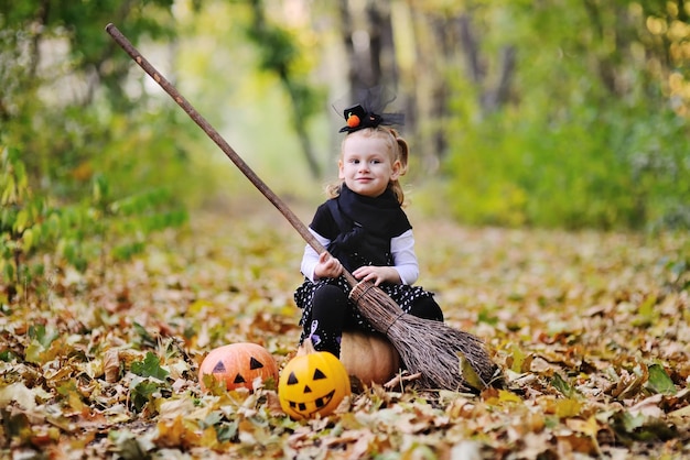 Een klein meisje verkleed als een heks op een bezemsteel op de achtergrond van het herfstbos viert Halloween