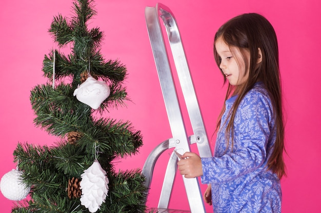 Een klein meisje versiert kerstboom op roze