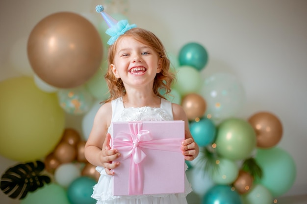 Een klein meisje viert haar verjaardag op de achtergrond van ballonnen met een geschenk