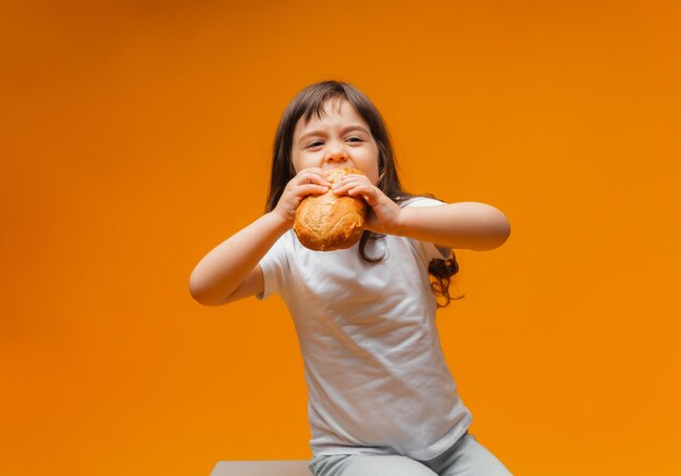 Een klein meisje zit op een kubus op een gele achtergrond en eet een brood gezond voedsel natuurlijke producten brood