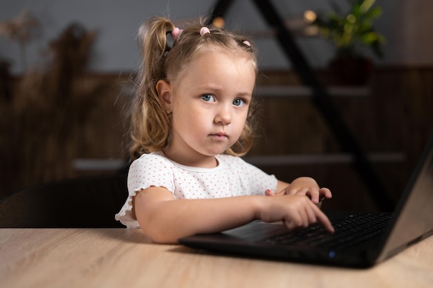 Een klein meisje zit 's avonds achter een laptop en typt Portret van een kleuter