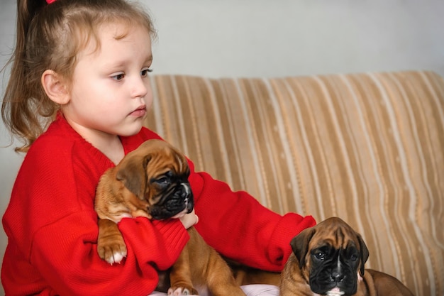 een klein meisje zit thuis op de bank en speelt met kleine puppy's