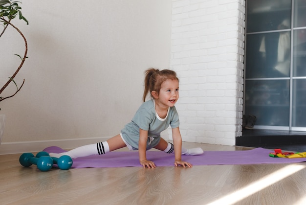 Een klein meisje zit thuis op de spleten tijdens een fitnessles