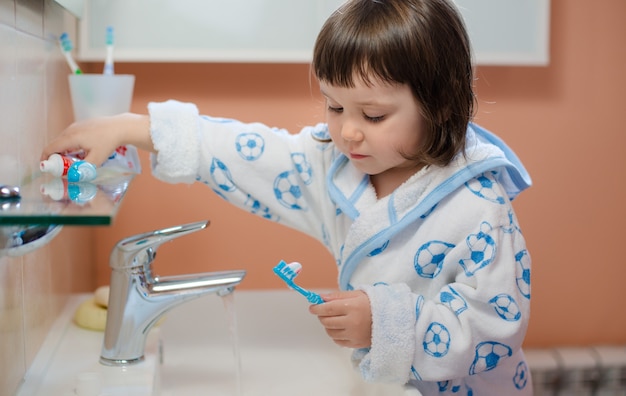 Een klein meisjeskind poetst tanden in de badkamer. Hygiëne van de mondholte.