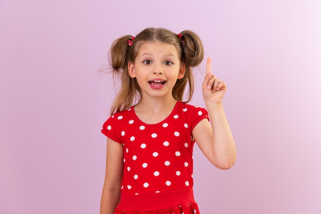 Een klein mooi meisje in een rode jurk wijst met haar vinger naar de bovenkant. Geïsoleerde achtergrond.