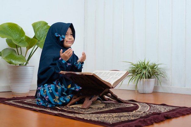 Een klein moslimmeisje bidt thuis op het gebedskleed op ramadan kareem met haar koran