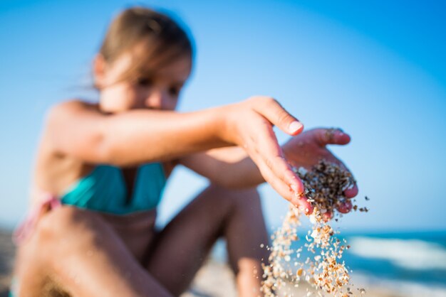 Een klein positief meisje zit aan de kust en geniet van de golven van de zee op een zonnige zomerdag tijdens vakantie. Concept van gezinsvakanties met kinderen