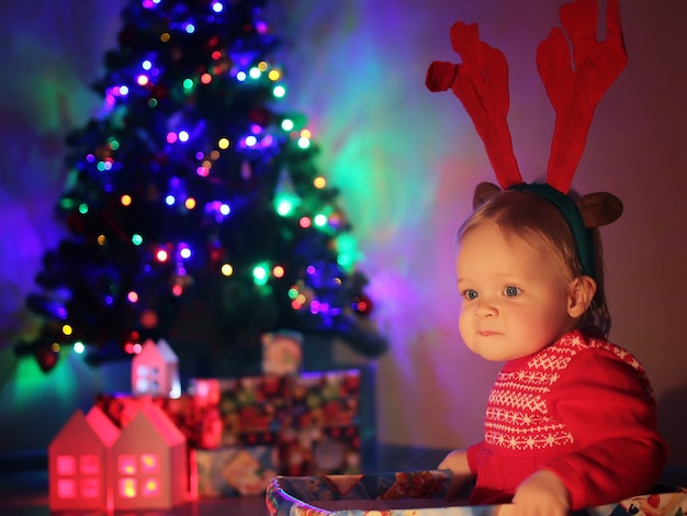 Een klein schattig babymeisje, met kerst herten hoorns, zit in een geschenkdoos