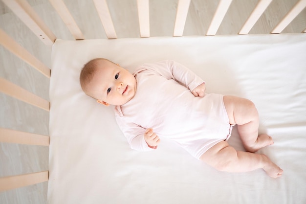 Een klein schattig glimlachend meisje in een witte bodysuit ligt in een wieg thuis op haar rug kijkend naar de camera glimlachende gelukkige baby