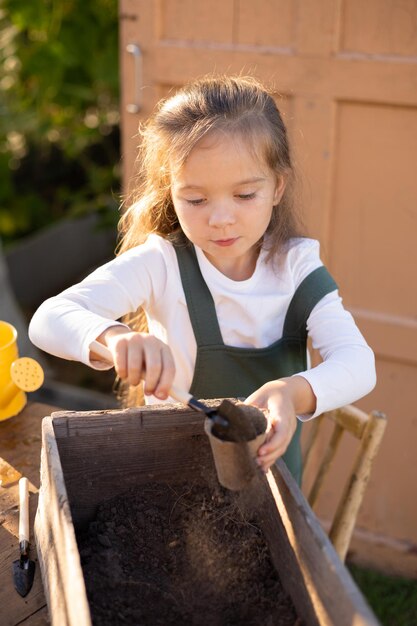 Foto een klein schattig langharig boerenmeisje houdt zich bezig met het planten van planten in de moestuin van het dorp