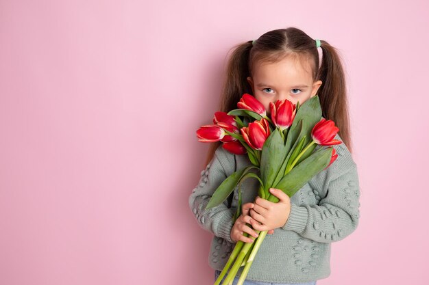 Een klein schattig meisje dat een boeket tulpen vasthoudt en eraan snuffelt Roze achtergrond Happy