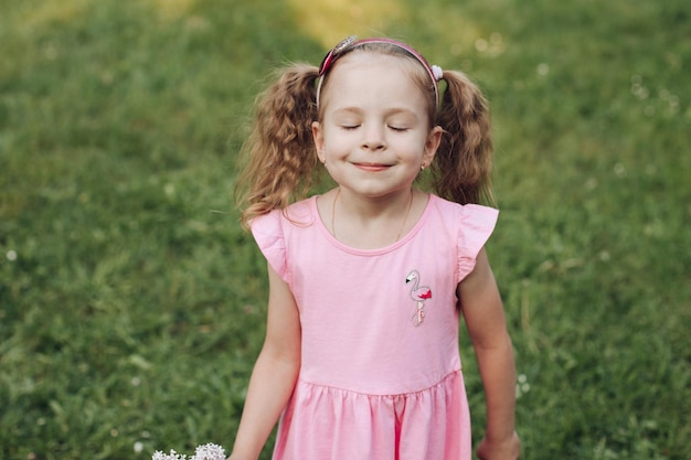 Een klein schattig meisje in een roze jurk in een groen park in de lente of zomer