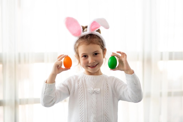 Een klein schattig meisje met konijnenoren houdt kleurrijke eieren in haar handen Pasen