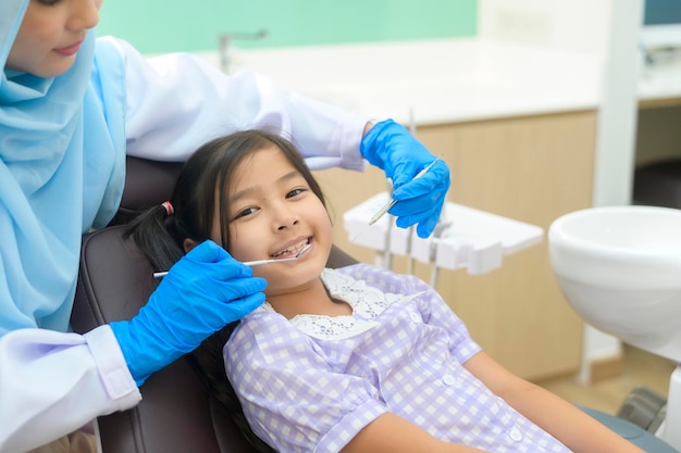 Een klein schattig meisje met tanden onderzocht door moslim tandarts in tandheelkundige kliniek tandencontrole en gezond gebit concept