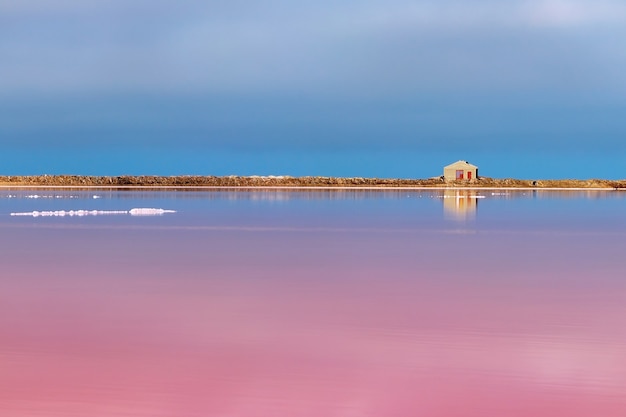 Een klein verlaten stenen huis staat op een roze zoutmeer onder een helderblauwe lucht