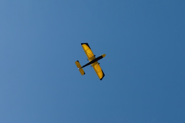 Een klein vliegtuig met gele vleugels in de lucht.