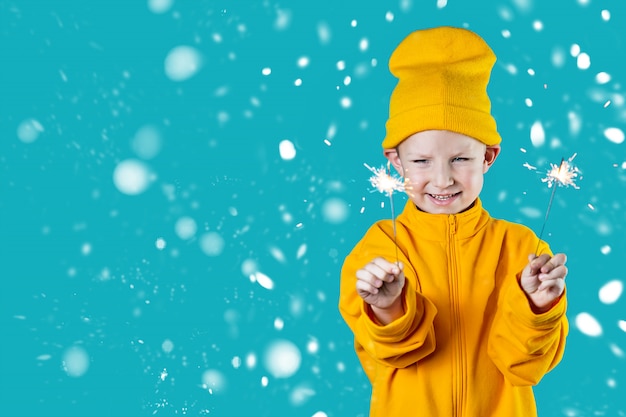 Een klein vrolijk kind in een gele hoed en jas houdt brandende sterretjes vast