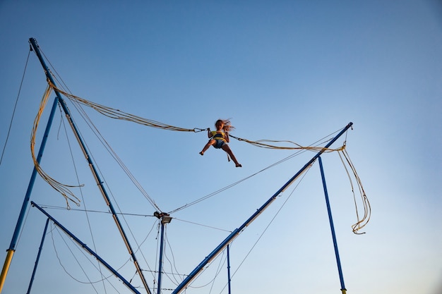 Een klein vrolijk meisje vliegt op verende, heldere elastische banden en springt op een trampoline, genietend van de langverwachte vakantie in de warme zon