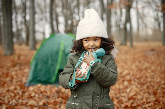 Een klein zwart meisje in tent kamperen in het bos Meisje houdt een thermoskan in haar handen Zwart meisje met een kaki jas en beige hoed