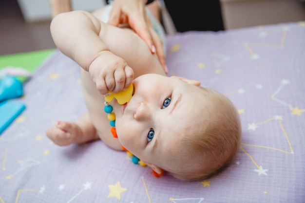 Een kleine baby die op zijn zij ligt krijgt een massage in een massageruimte hij heeft een speeltje in zijn mond