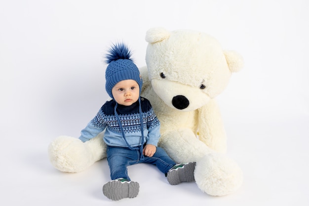 een kleine babyjongen in een warme wintermuts met een pompon en een blauw jasje zit op wit