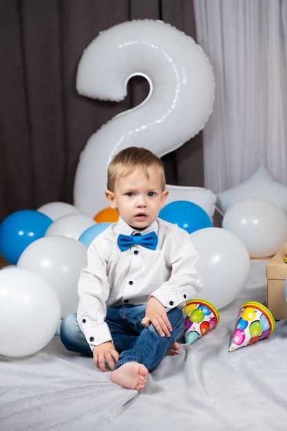 Foto een kleine blonde jongen met blauwe ogen viert zijn verjaardag tussen opblaasbare ballonnen