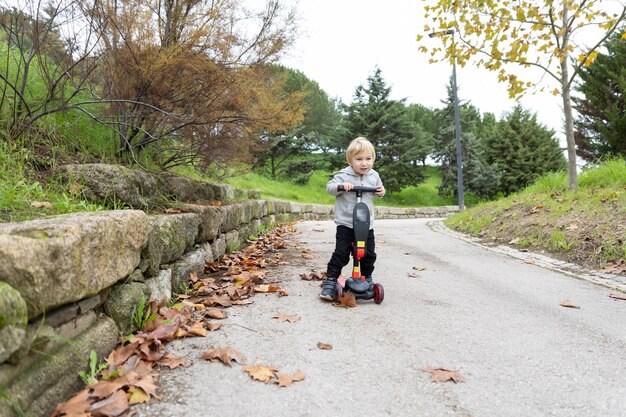 Een kleine blonde jongen rijdt op een scooter in het herfstpark