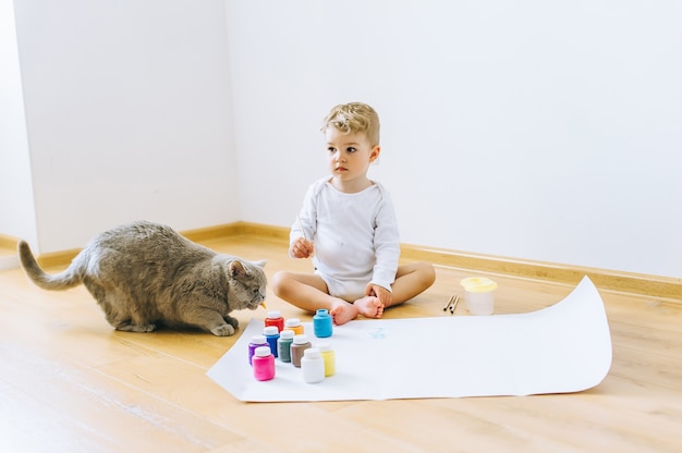 een kleine blonde jongen schildert een papier met een kat