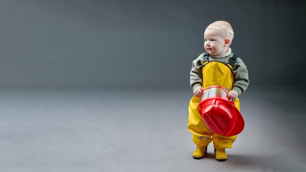 Een kleine eenjarige baby in brandweerpak met helm in zijn handen