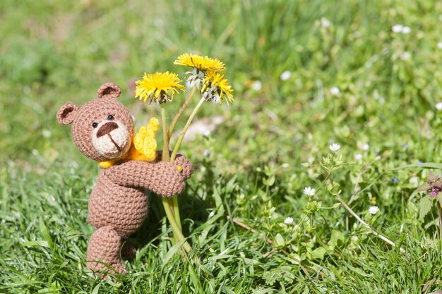 Een kleine gebreide bruine beer met een gele sjaal in de zomertuin. Gebreide speelgoed, handgemaakte, amigurumi