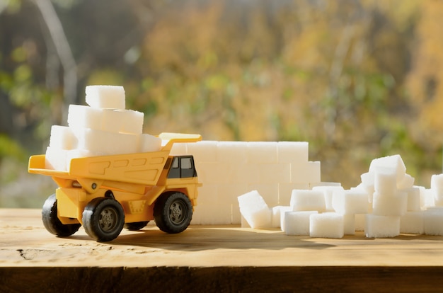 Een kleine gele speelgoedtruck staat vol met witte suikerklontjes in de buurt van de suikerresten.