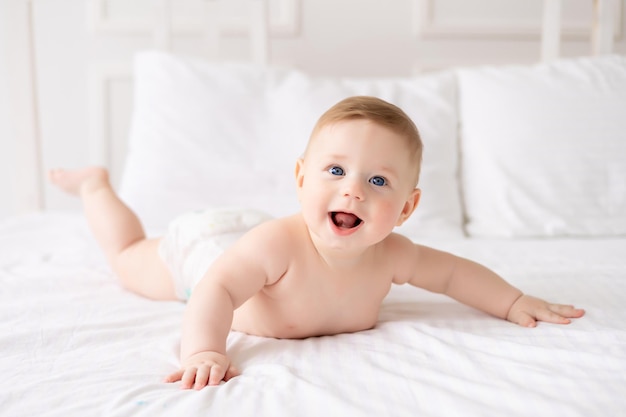 Een kleine gezonde baby in een luier ligt thuis op wit beddengoed Gelukkige baby liggend op zijn buik textiel en beddengoed voor kinderen