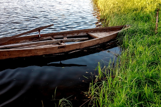 Een kleine houten roeiboot met een gebroken bodem op een kalm meer dichtbij de kust.