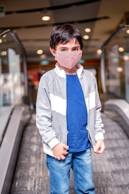 Een kleine jongen beklimt de roltrappen van een warenhuis met een beschermend masker op