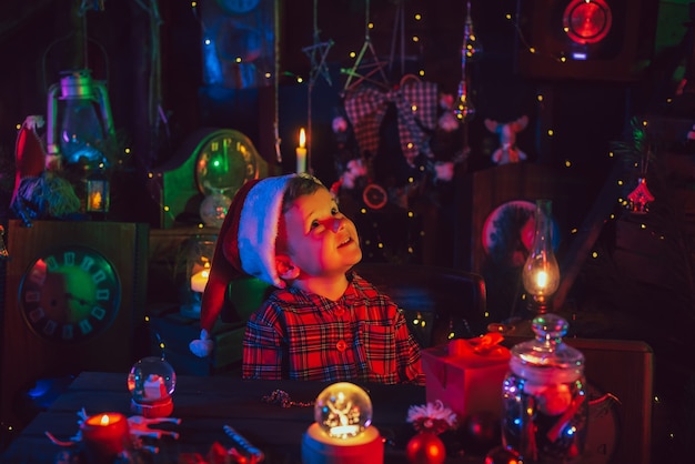 Een kleine jongen, de assistent van de Kerstman, zit aan een tafel met cadeaus in fantastische kerstversieringen. Ansichtkaart.