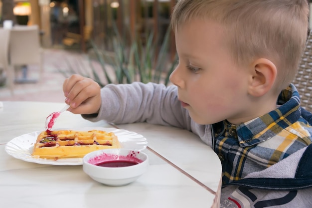 Een kleine jongen eet belgische dessertwafels met jam in een café