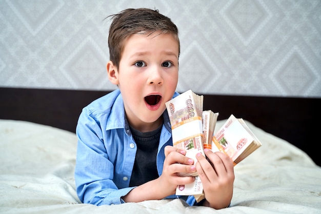 Foto een kleine jongen houdt biljetten van vijfduizend dollar in zijn handen boven een bed