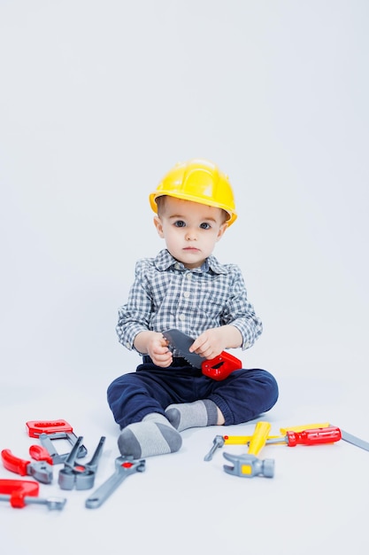 Een kleine jongen in een geruit hemd in de afbeelding van een bouwer Een jongen in een bouwhelm en plastic gereedschap