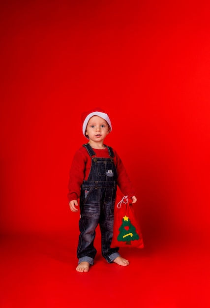 Een kleine jongen in een jumpsuit van spijkerstof en een nieuwjaarsmuts staat