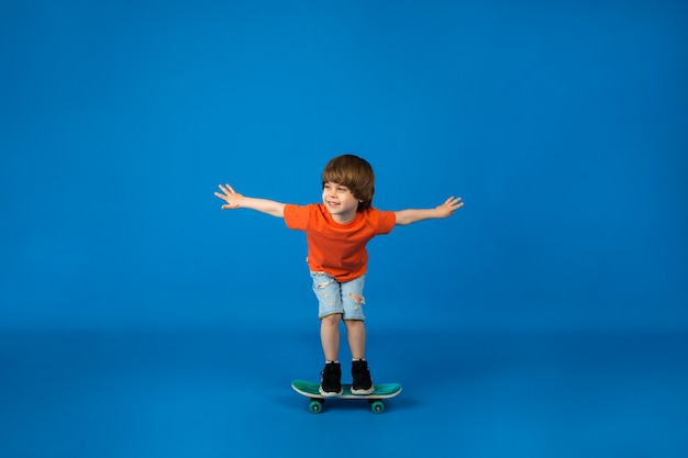 Een kleine jongen in een T-shirt en korte broek rijdt op een skateboard op een blauwe ondergrond met ruimte voor tekst