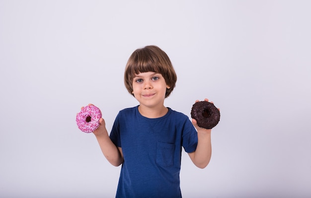 Een kleine jongen in een T-shirt houdt donuts vast op een witte achtergrond met een kopie van de spatie