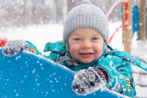 Een kleine jongen in een warme jumpsuit speelt in de winter buiten op de speelplaats.