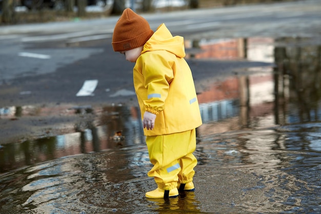 Een kleine jongen in een waterdicht pak loopt door plassen