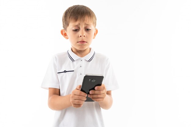 Een kleine jongen in een wit overhemd, blauwe korte broek met blond haar, zwarte bril met telefoon