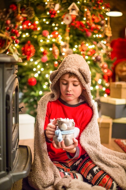 Een kleine jongen in kerstpyjama zit in de buurt van een kerstboom