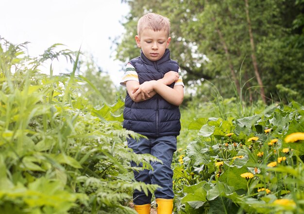 Foto een kleine jongen in rubberen laarzen loopt door een struikgewas en wordt gebeten door muggen